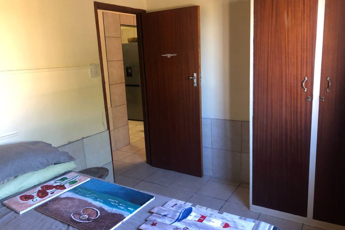 A bedroom featuring tiled flooring and a built-in wooden wardrobe, with an adjoining doorway leading to another room.