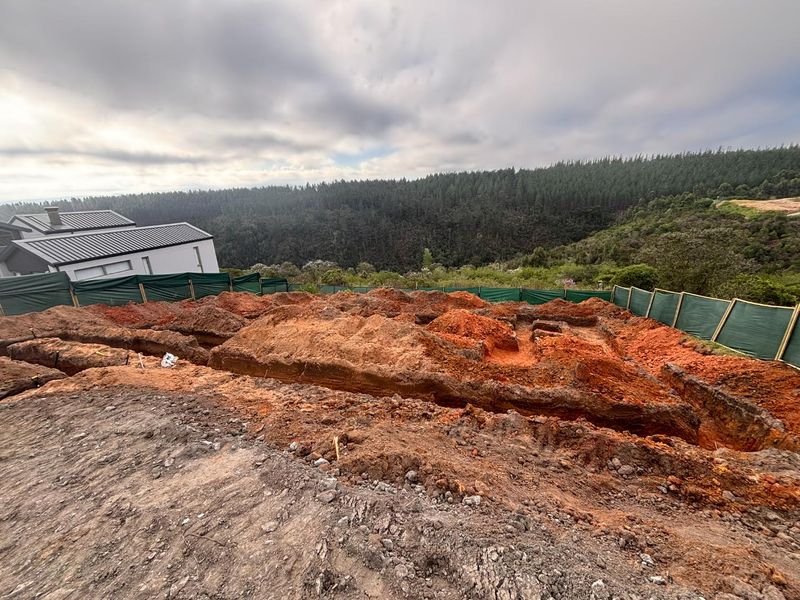 A construction site showing excavated foundation trenches for a new residential build, set against a scenic forest backdrop.