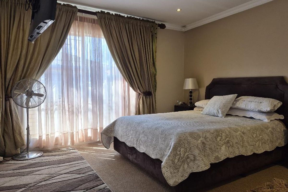 A carpeted bedroom featuring recessed downlights, decorative ceiling cornice, and a large sliding glass door with floor-to-ceiling curtains providing natural light.
