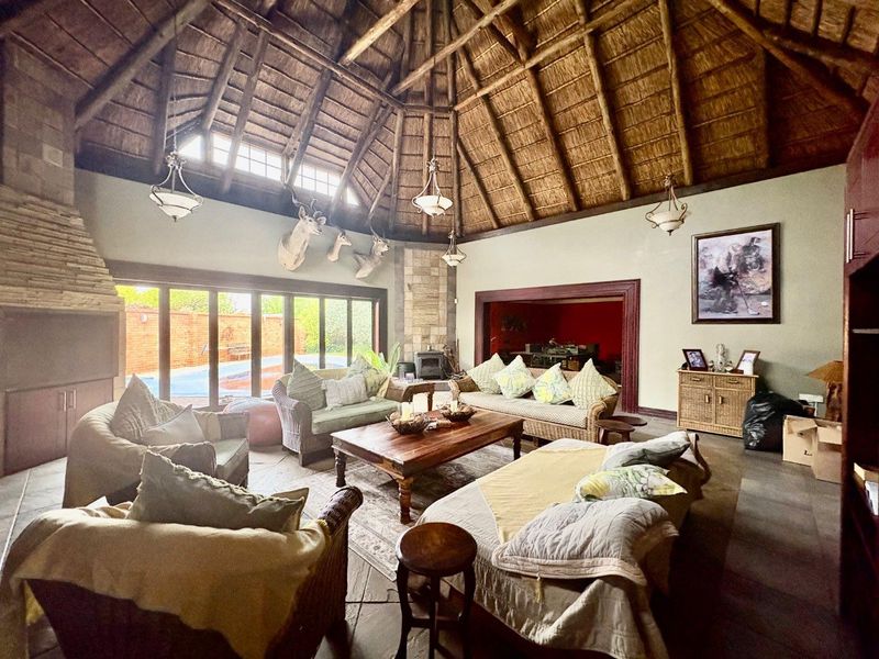 Spacious living room featuring a high vaulted thatched ceiling with exposed timber rafters, a stone fireplace, and large sliding doors opening to the pool area.