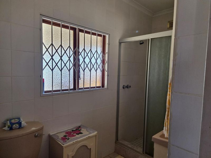 A functional bathroom featuring a shower enclosure, tiled walls, and a window with security bars, offering potential for modernization.