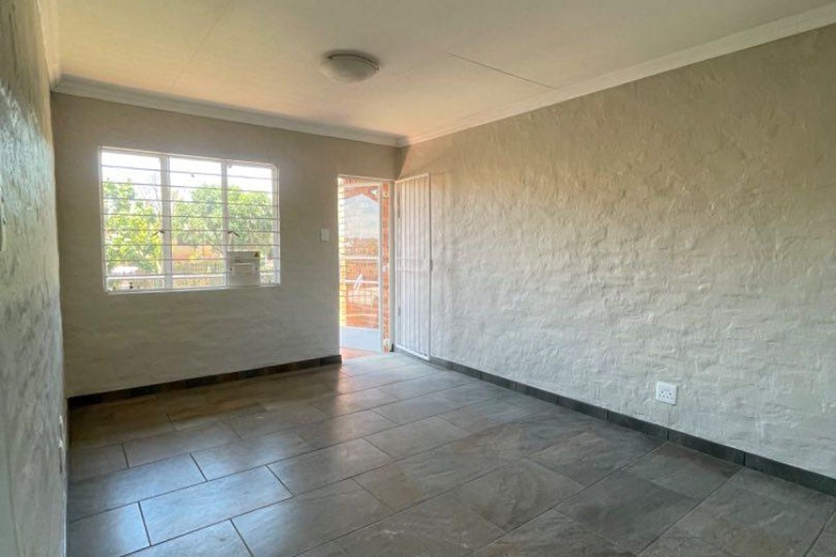 An empty living room featuring neutral textured brick walls and large format floor tiles, with natural light entering through a window and exterior door.