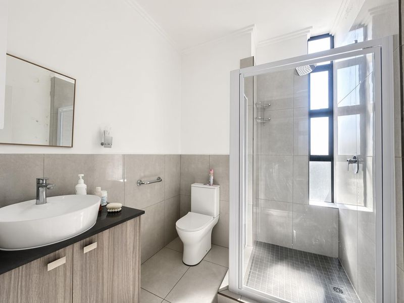 Modern bathroom featuring a vanity with vessel sink, a toilet, and a glass-enclosed shower with neutral grey tiling.