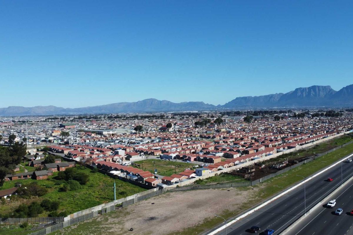 An aerial view of a residential neighborhood situated near a major highway, featuring mountain views in the background.