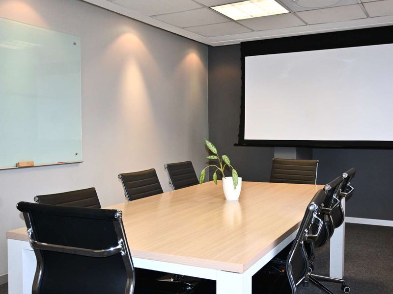 A professional office meeting room featuring a large conference table, wall-mounted glass whiteboard, and a retractable projector screen for presentations.