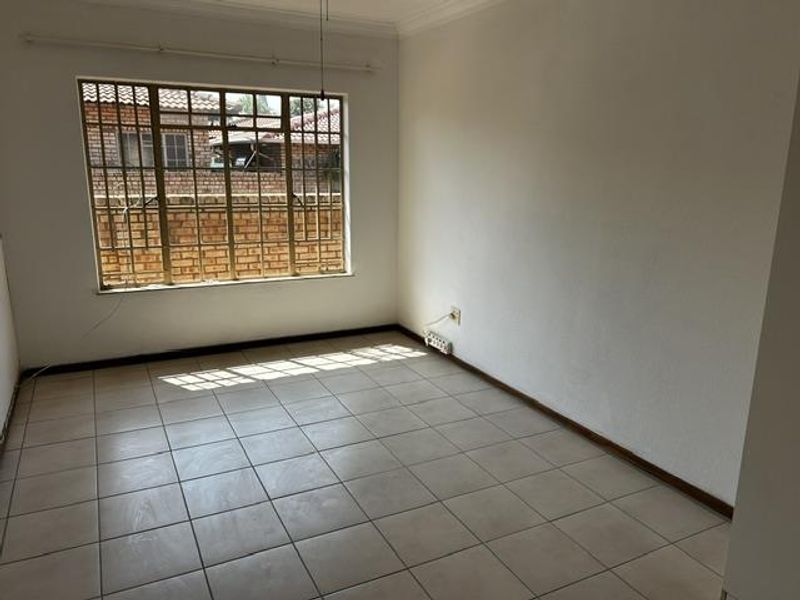 An empty, neutrally painted living room featuring tiled flooring and a large window with security bars, offering a blank canvas for personalization.
