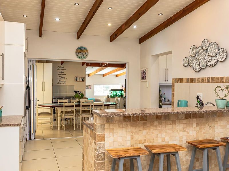 Open-plan kitchen and dining area featuring granite countertops, a tiled breakfast bar, and exposed timber ceiling beams, creating a warm and functional living space.