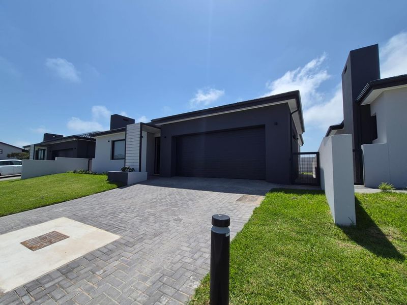 Modern single-story residential facade featuring a paved driveway, automated garage, and clean architectural lines with well-maintained lawn areas.