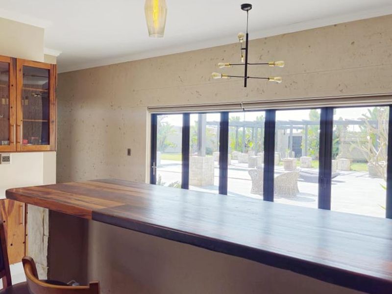 Open plan living area featuring a custom wooden bar counter, modern pendant lighting, and large bi-fold doors opening to an outdoor patio space.