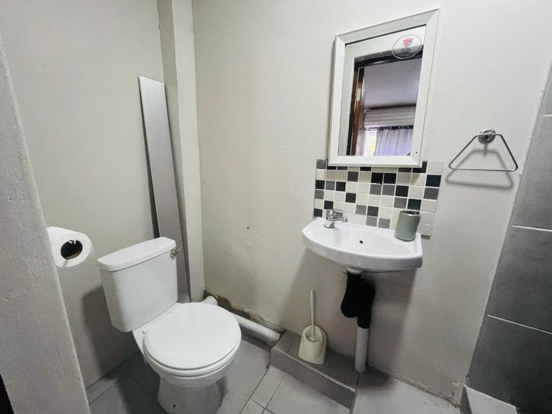 A compact bathroom featuring a standard toilet, wall-mounted basin with a tiled splashback, and a mirror, requiring some cosmetic updates to the wall finishes.
