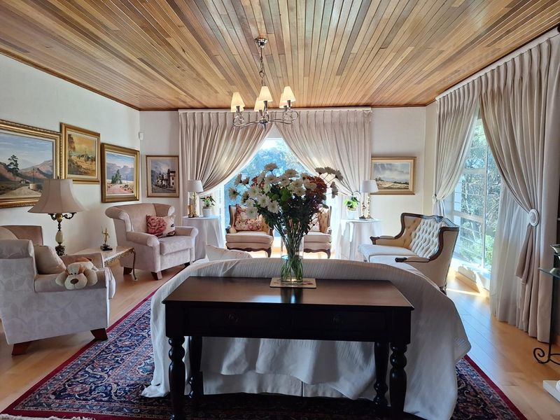 A spacious and elegant living room featuring a warm timber tongue and groove ceiling, large windows with natural light, and polished hardwood flooring.