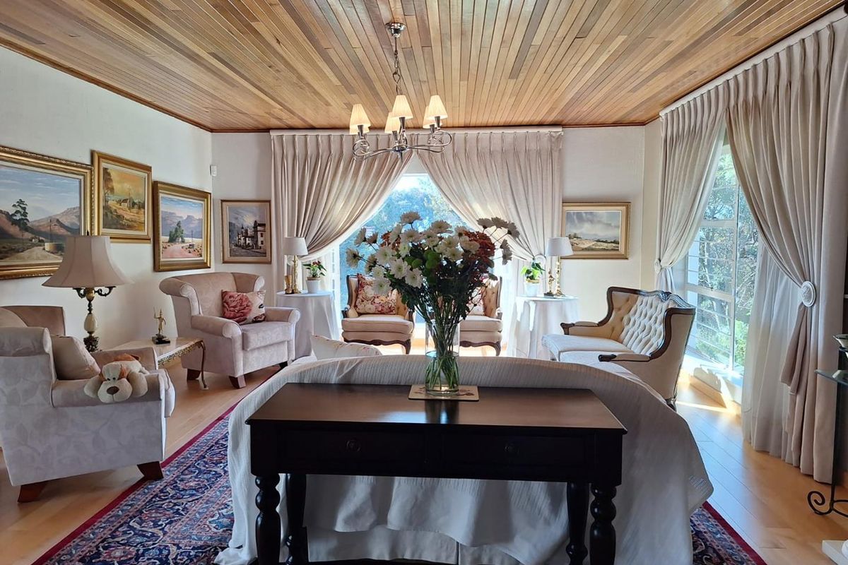 A spacious and elegant living room featuring a warm timber tongue and groove ceiling, large windows with natural light, and polished hardwood flooring.