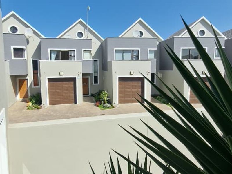 A view of the front elevation of a townhouse complex featuring multiple units with individual garages, paved driveways, and modern pitched roof architecture.