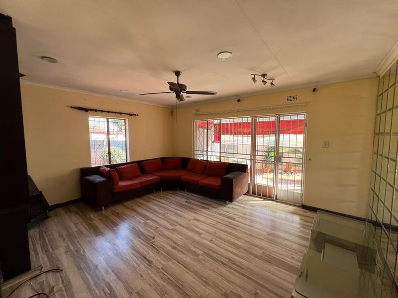 Spacious living room featuring laminate flooring, ceiling fan, recessed lighting, and a glass block feature wall with access to the outdoor area.
