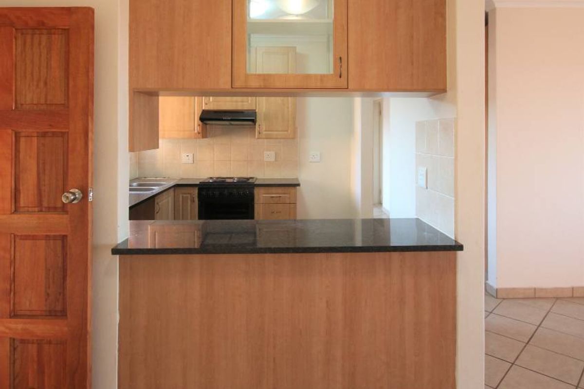 A functional kitchen featuring light wood cabinetry, granite countertops, a breakfast bar, and tiled flooring, offering a clean and practical layout.