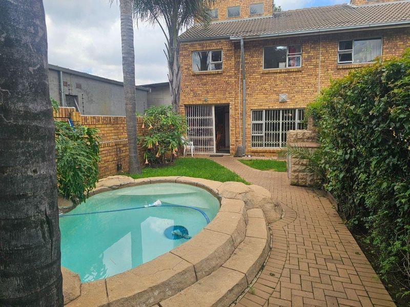 Rear exterior view of a townhouse featuring a small swimming pool, brick paved pathway, and a private garden area with brick boundary walls.