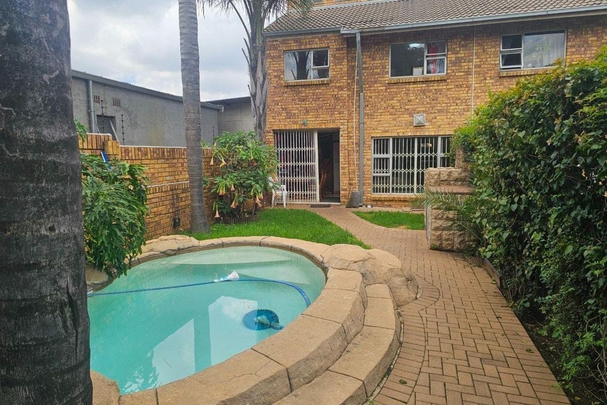 Rear exterior view of a townhouse featuring a small swimming pool, brick paved pathway, and a private garden area with brick boundary walls.
