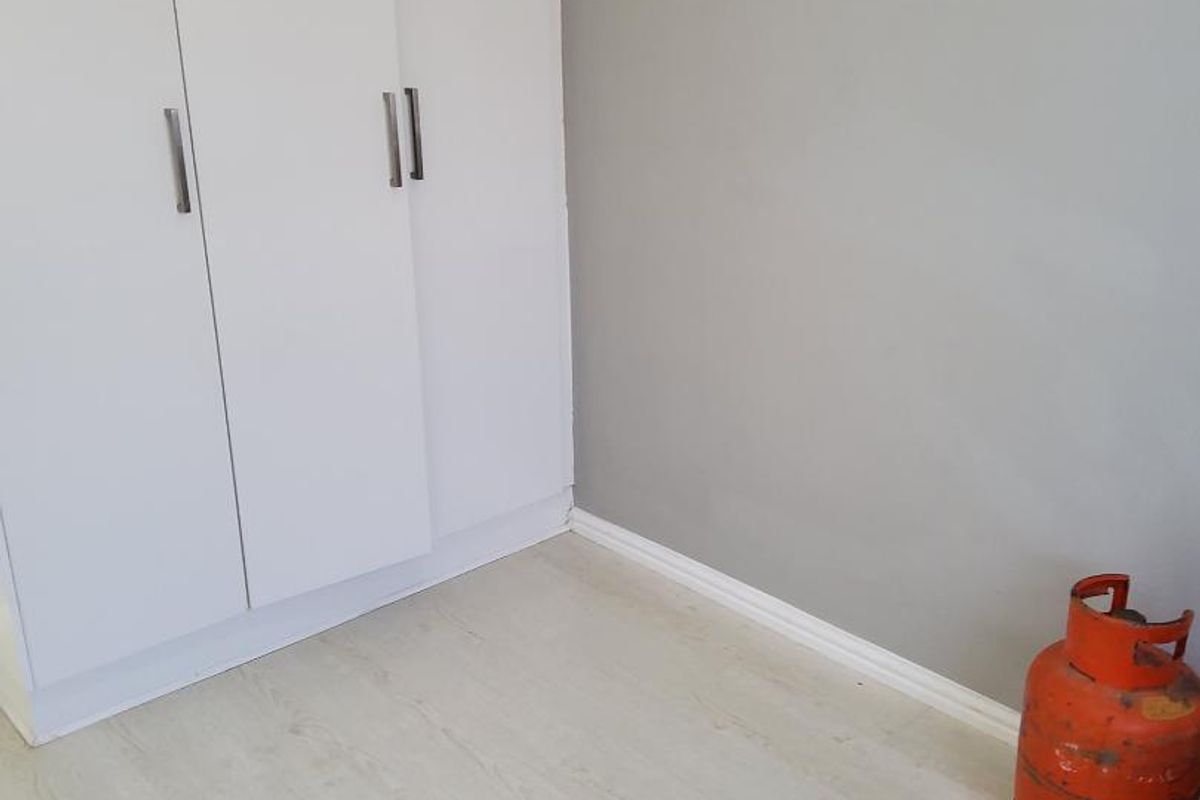 A bedroom featuring light-toned laminate flooring and built-in white cabinetry with modern handles.