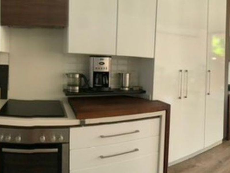 A bright open-plan living and kitchen area featuring modern white cabinetry, stainless steel appliances, and direct access to a private outdoor patio space.