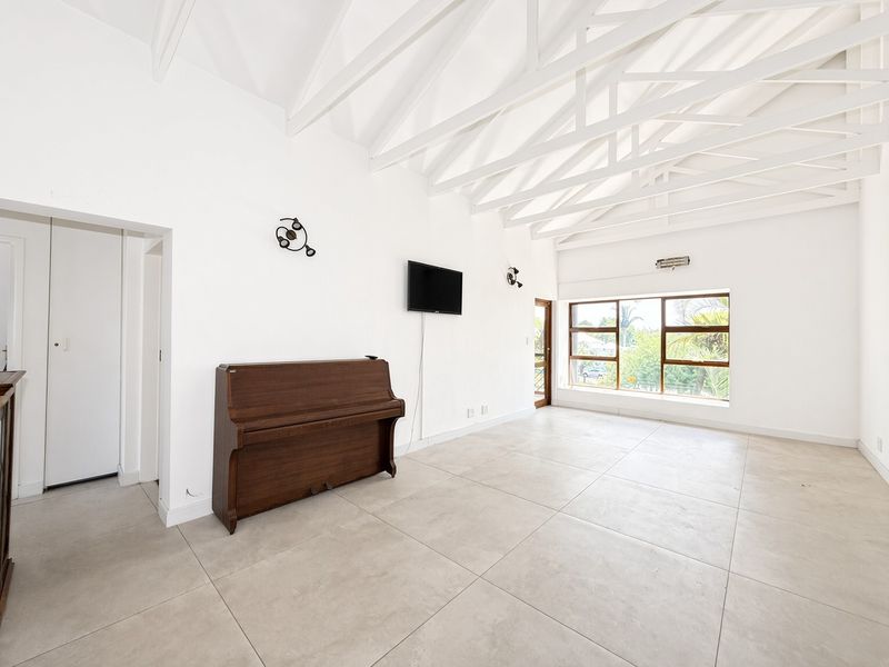 Spacious living area featuring high vaulted ceilings with exposed white timber trusses, large windows for natural light, and neutral tiled flooring throughout.