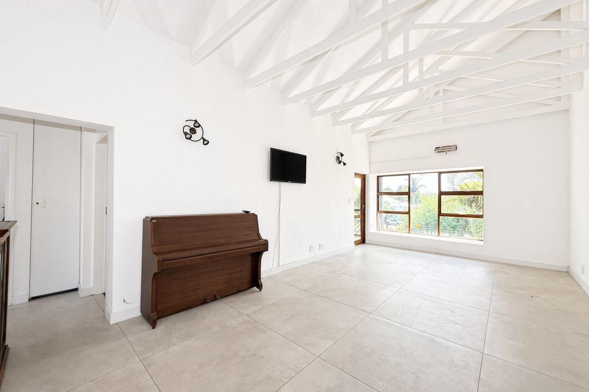 Spacious living area featuring high vaulted ceilings with exposed white timber trusses, large windows for natural light, and neutral tiled flooring throughout.