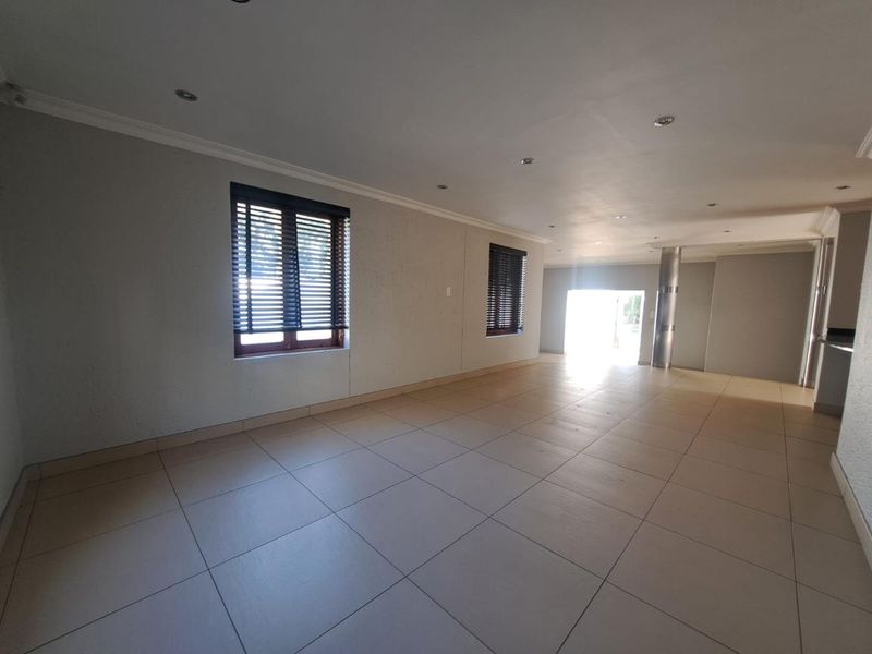 Spacious open-plan living area featuring neutral tiled flooring, recessed lighting, and large windows with fitted blinds, offering a bright and versatile layout.