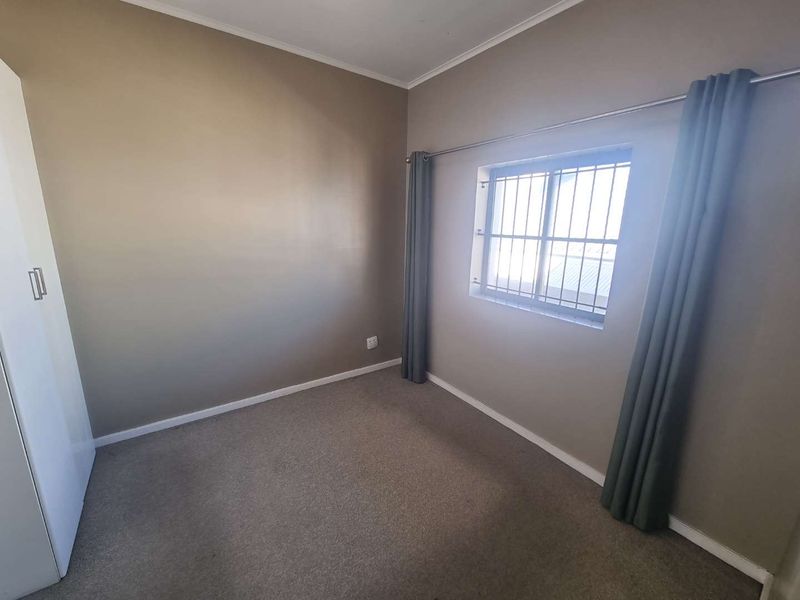 A clean, empty bedroom featuring neutral wall tones, carpet flooring, and a built-in wardrobe with security bars on the window.