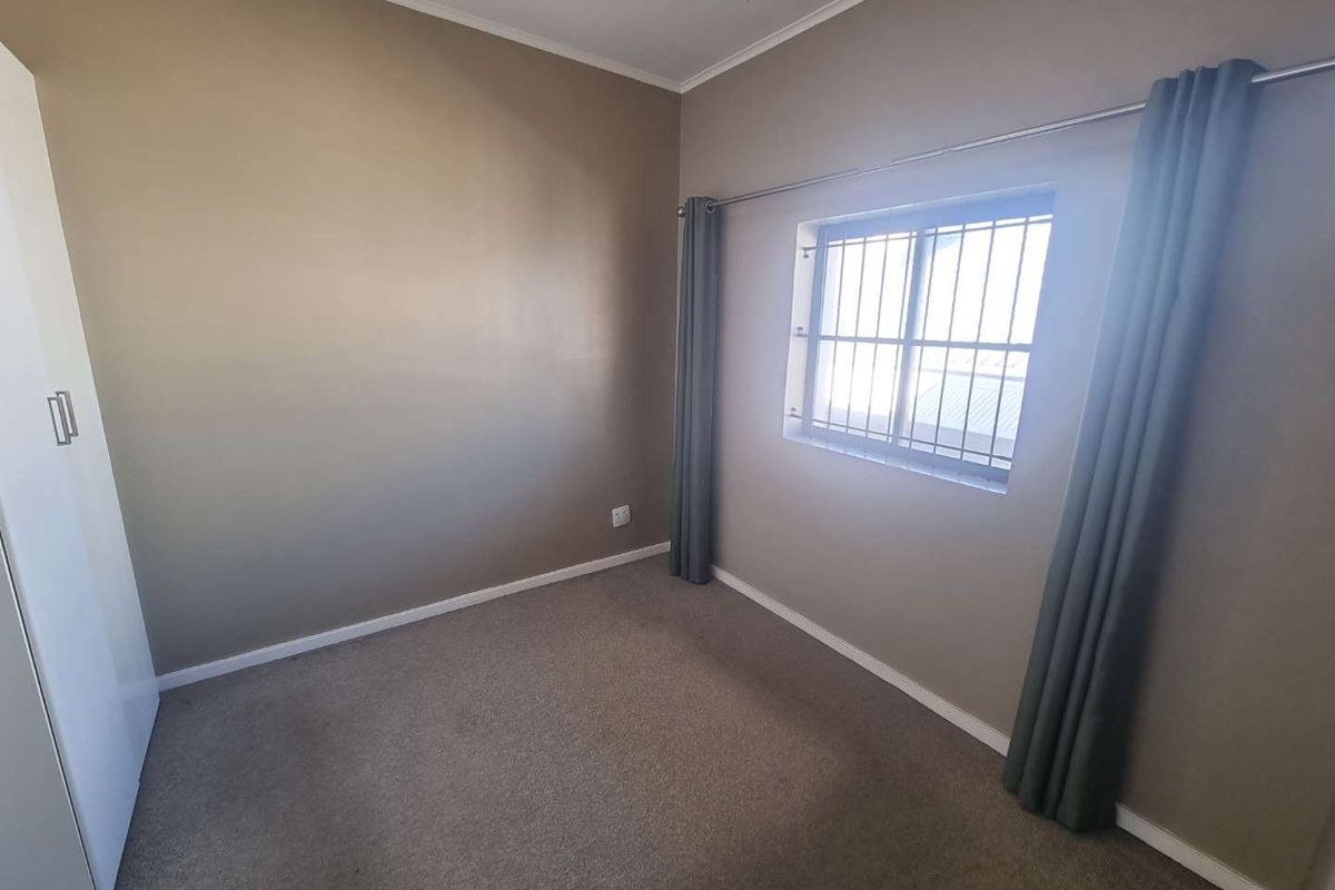A clean, empty bedroom featuring neutral wall tones, carpet flooring, and a built-in wardrobe with security bars on the window.
