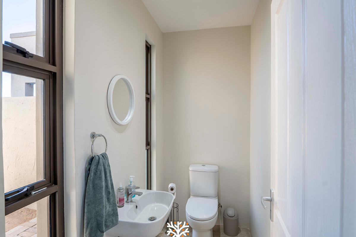 A modern guest bathroom featuring a wall-mounted basin, a dual-flush toilet, and large windows providing natural light.
