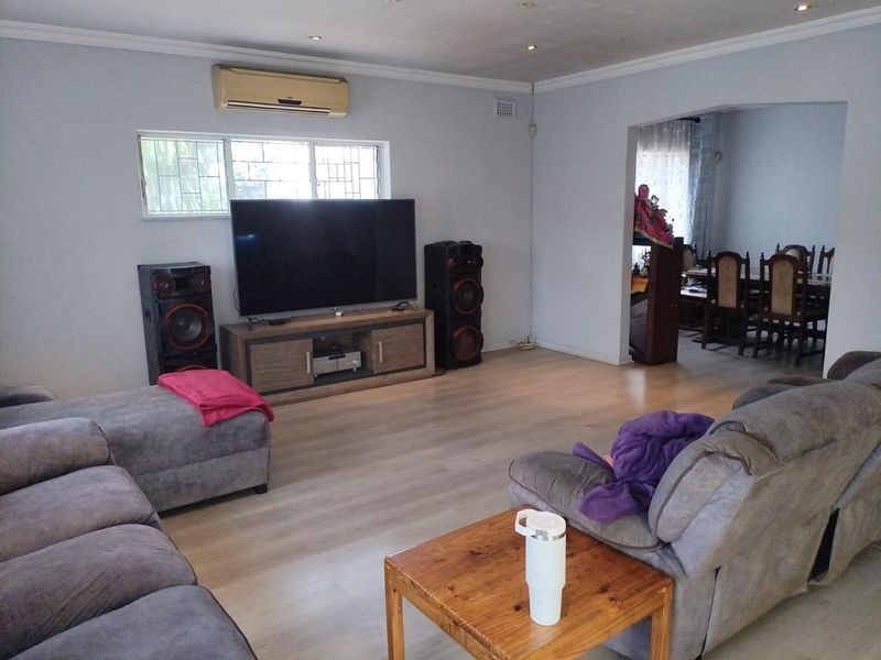 Spacious living room featuring light-toned laminate flooring, recessed downlighting, and a wall-mounted air conditioning unit, with an open-plan flow into the adjacent dining area.