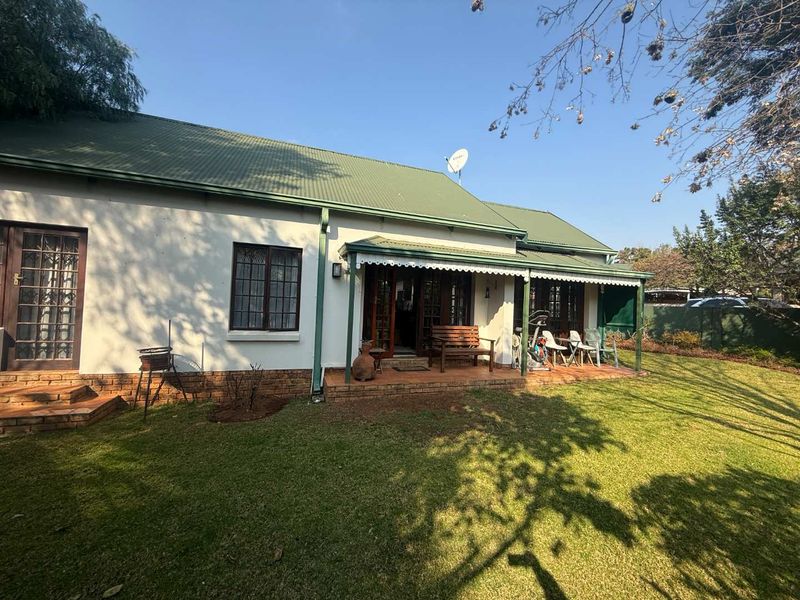 Rear view of the property featuring a covered patio, brick paving, and a well-maintained garden with a corrugated metal roof.