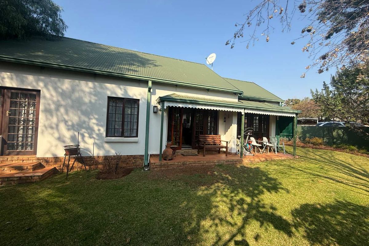 Rear view of the property featuring a covered patio, brick paving, and a well-maintained garden with a corrugated metal roof.