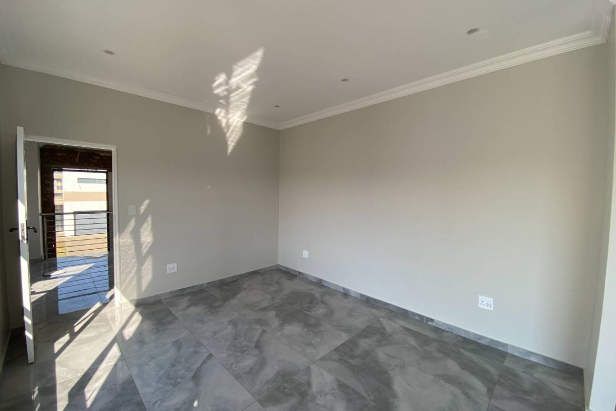 A bright, empty bedroom featuring modern grey tiled flooring, recessed downlighting, and neutral wall finishes, with access to an adjoining balcony.