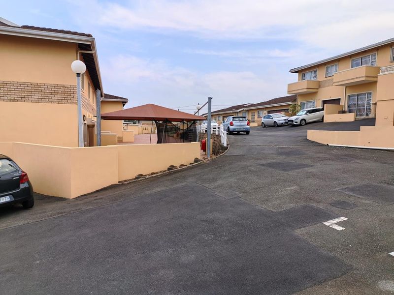 A view of the townhouse complex driveway and exterior facades, featuring paved access and established boundary walls.