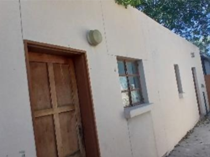 Rear exterior view of the industrial property featuring a paved walkway, boundary wall, and access door.