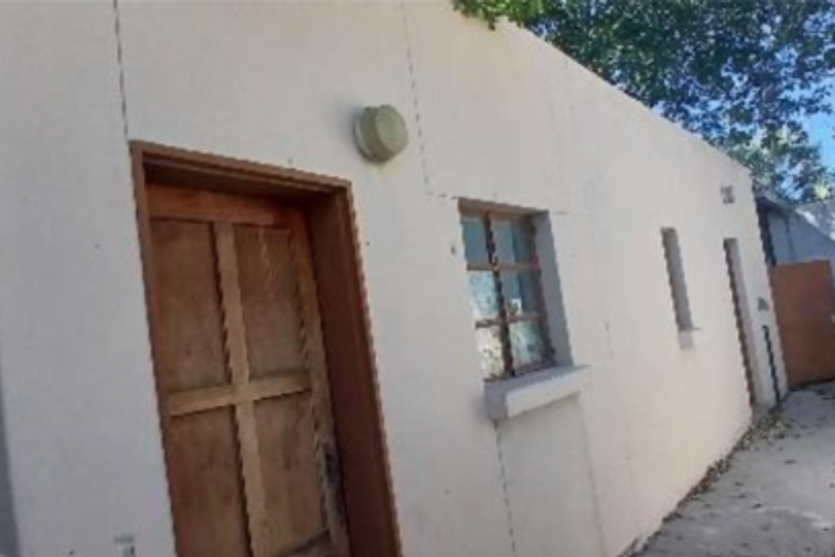 Rear exterior view of the industrial property featuring a paved walkway, boundary wall, and access door.