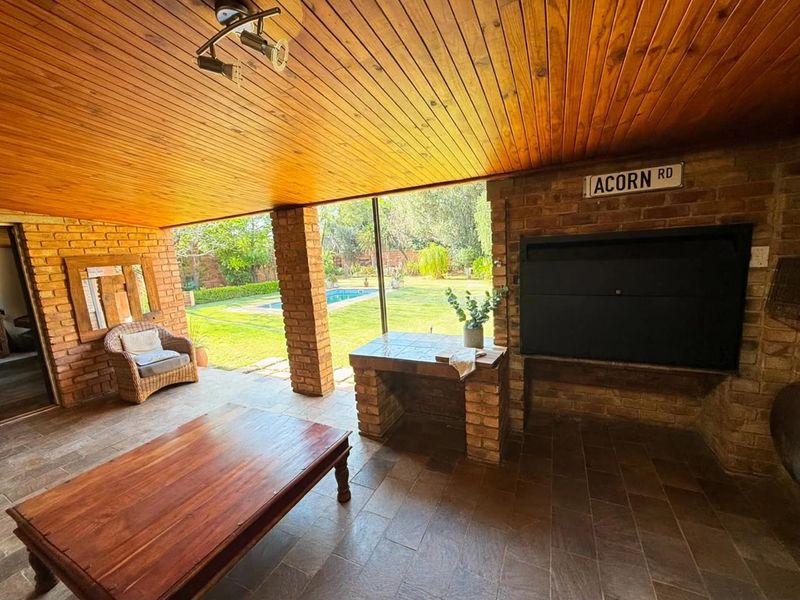Covered outdoor patio featuring a built-in braai, exposed timber ceiling, and brick accents, overlooking the garden and swimming pool area.