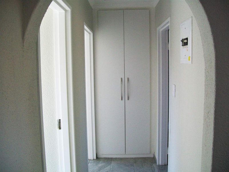 A clean, neutral hallway featuring tiled flooring, an arched entryway, and a built-in storage cupboard.
