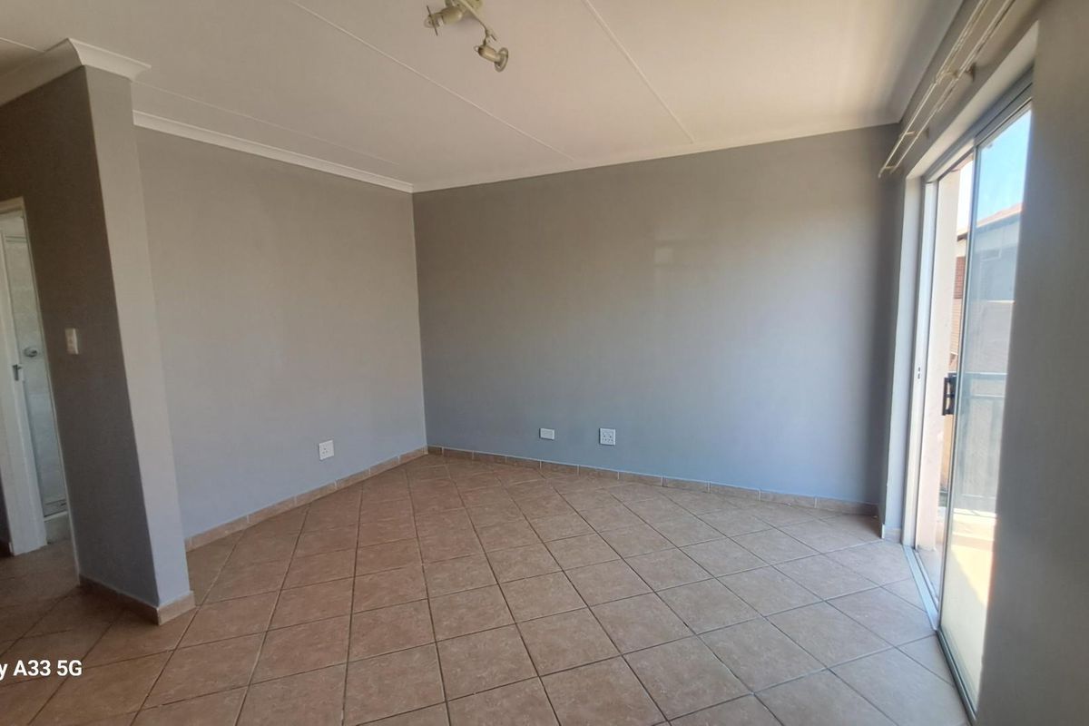 An empty living room featuring neutral grey walls, tiled flooring, and a sliding glass door providing access to an outdoor area.