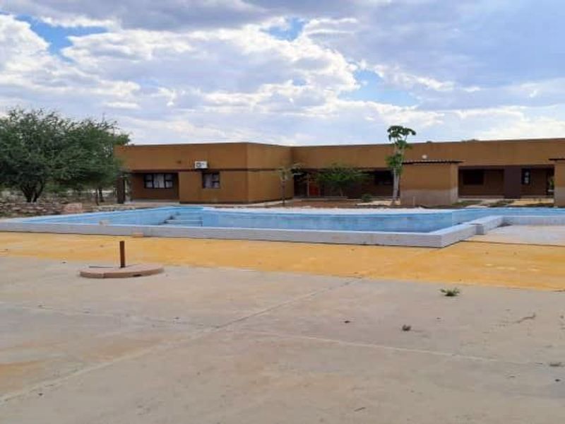 An outdoor pool area featuring a concrete deck and a single-story building with exterior wall finishes and an installed air conditioning unit.