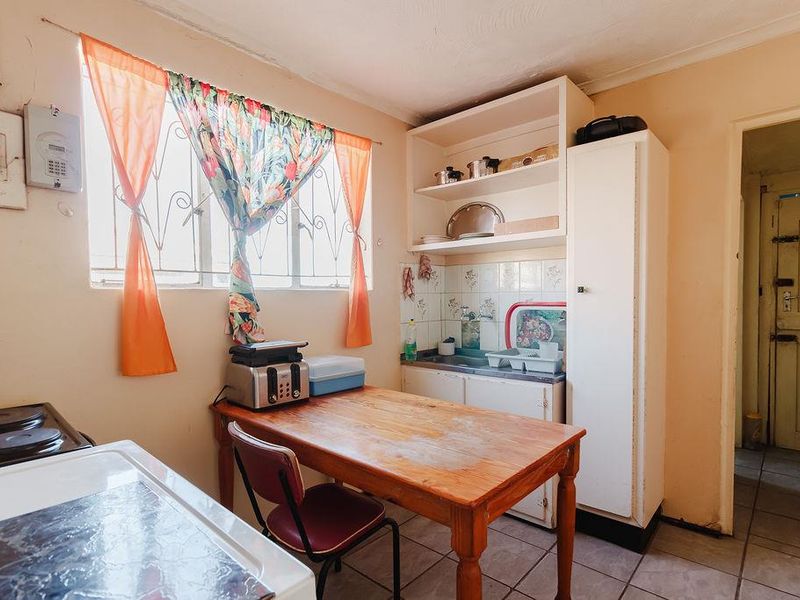 A functional kitchen area featuring built-in cabinetry, a sink, tiled backsplash, and tiled flooring, requiring cosmetic updates to modernize the space.