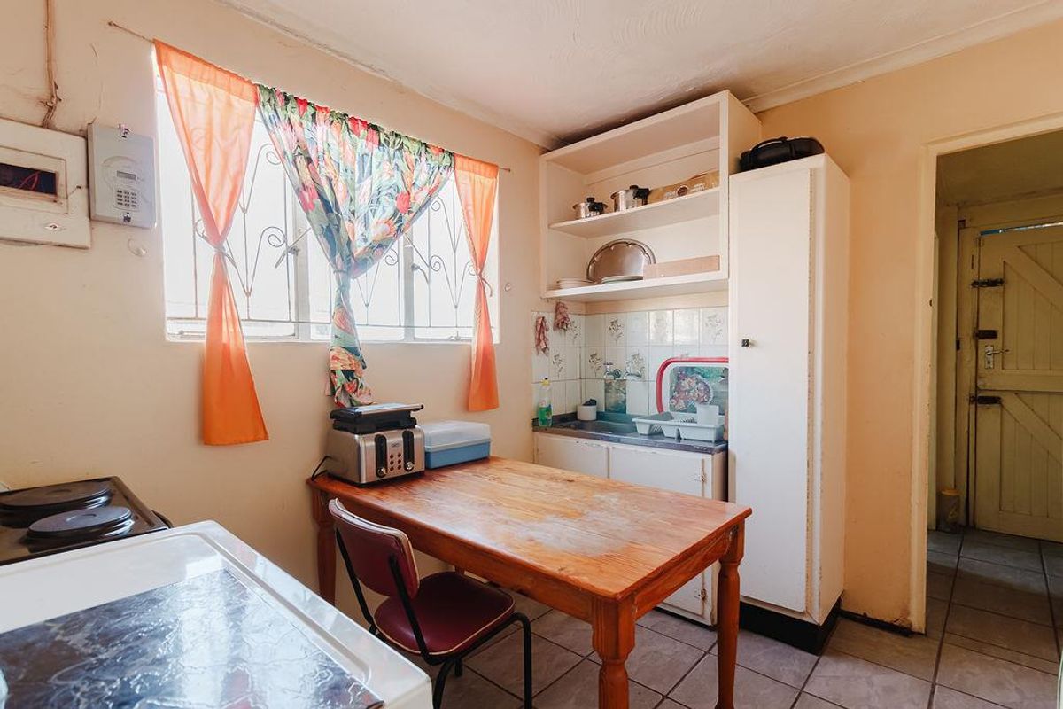 A functional kitchen area featuring built-in cabinetry, a sink, tiled backsplash, and tiled flooring, requiring cosmetic updates to modernize the space.