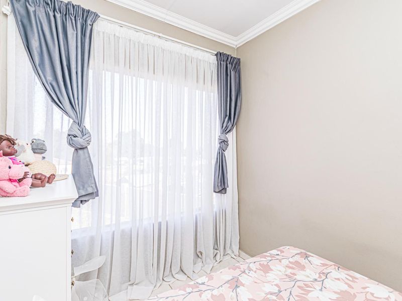 A bedroom featuring neutral wall tones, crown molding, and a large window with layered curtains, providing natural light to the space.