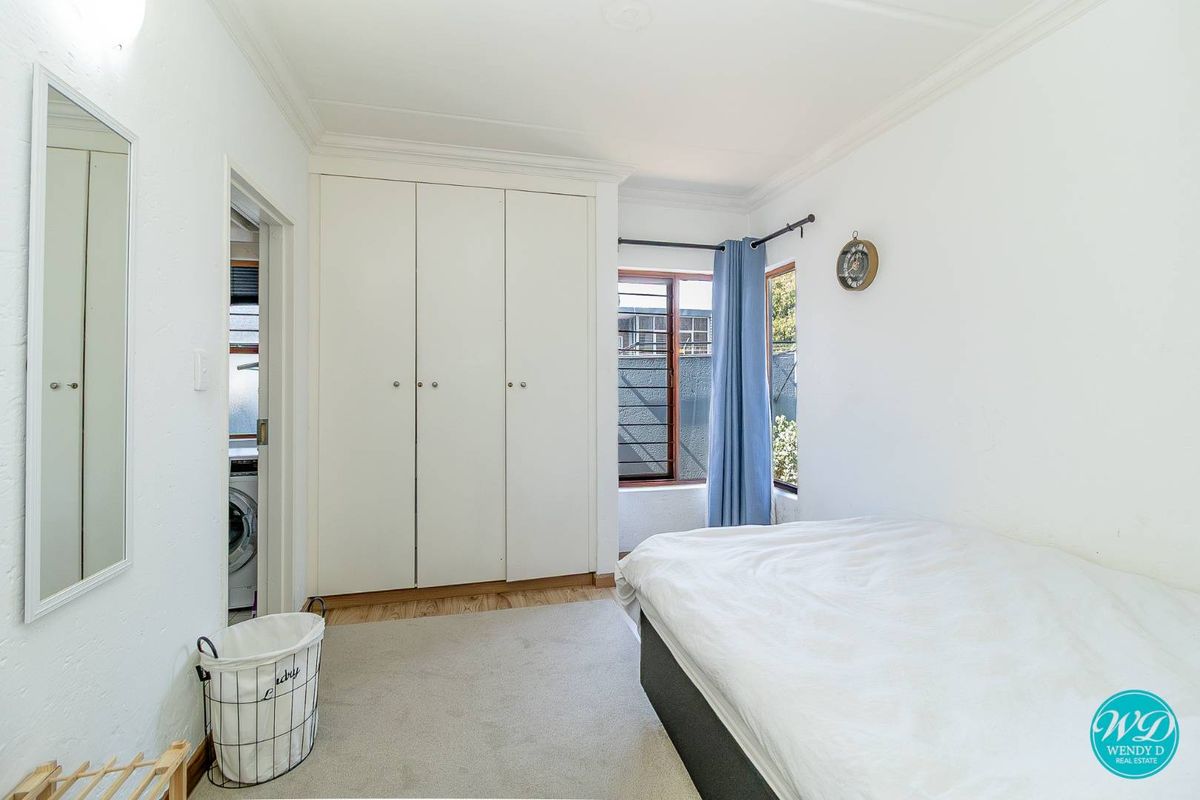 A bright bedroom featuring built-in cupboards, timber window frames, and classic cornicing, with an adjacent laundry area visible through the doorway.