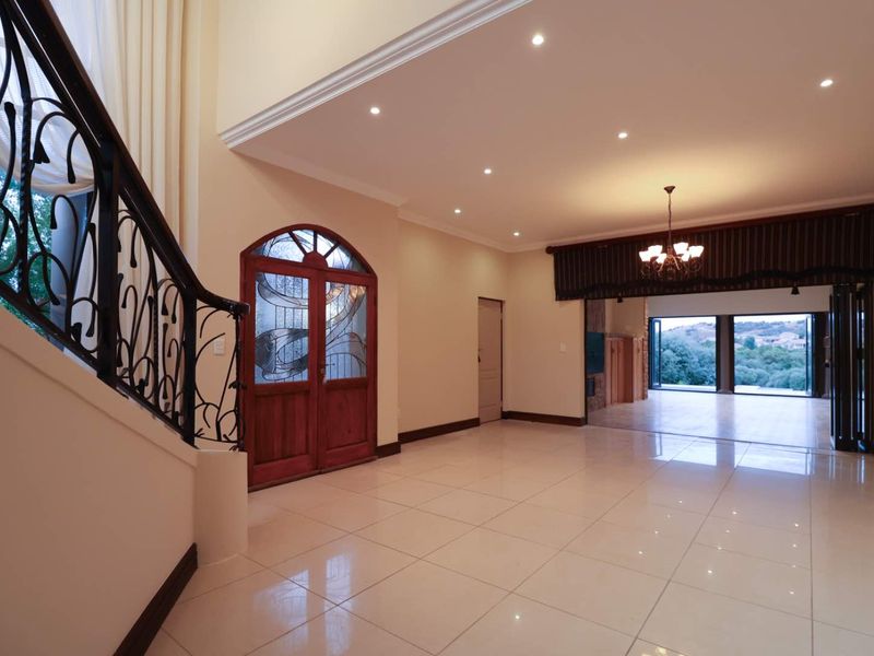 Spacious entrance hall featuring polished porcelain tiles, a decorative wrought iron staircase, and double wooden doors, leading into an open-plan living area.