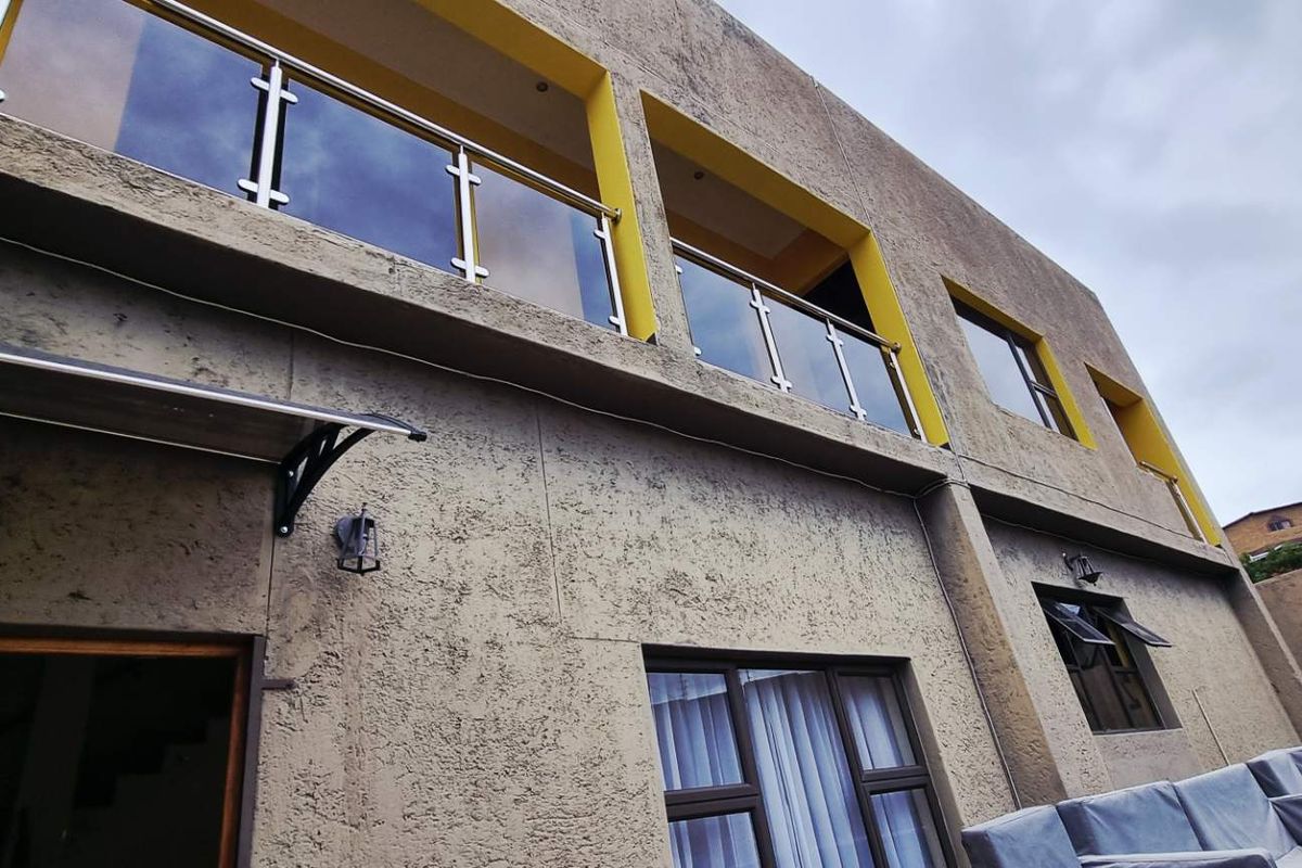 Rear view of the property featuring a balcony with glass and stainless steel balustrades, textured exterior walls, and ground floor access.