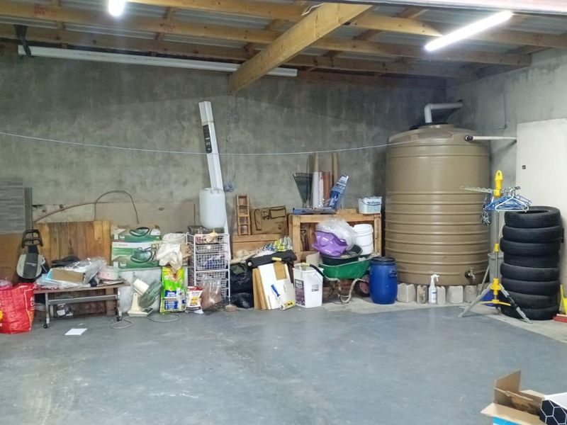 A functional garage space featuring exposed timber roof trusses, concrete flooring, and an integrated water storage tank.