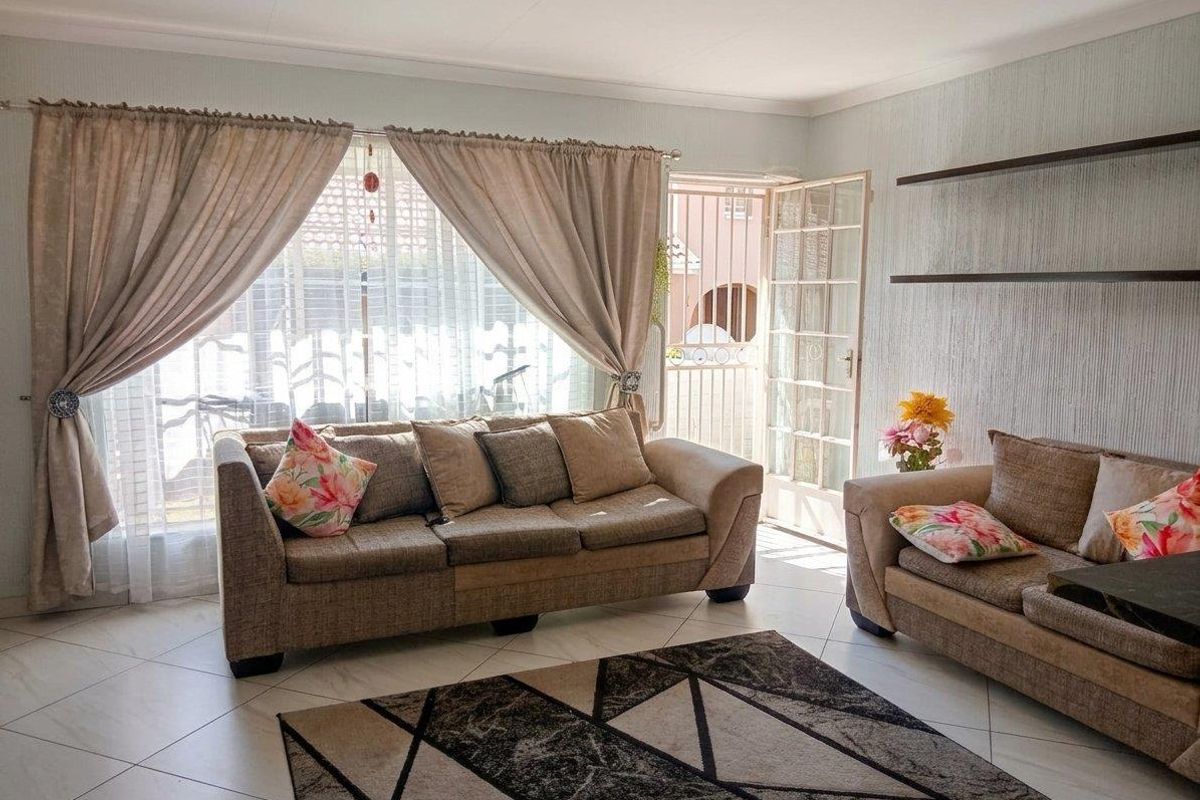 A bright living room featuring tiled flooring, floating wall shelves, and direct access to the exterior through a glass-paned door with a security gate.