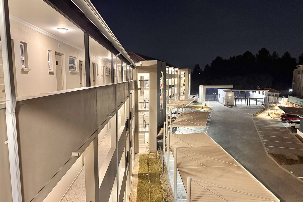 Night view of an apartment complex exterior featuring covered parking bays, a secure gated entrance, and well-lit external walkways.