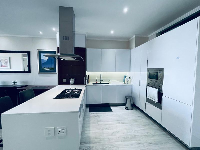 Modern kitchen featuring a central island with gas hob, integrated appliances, sleek white cabinetry, and contemporary finishes.